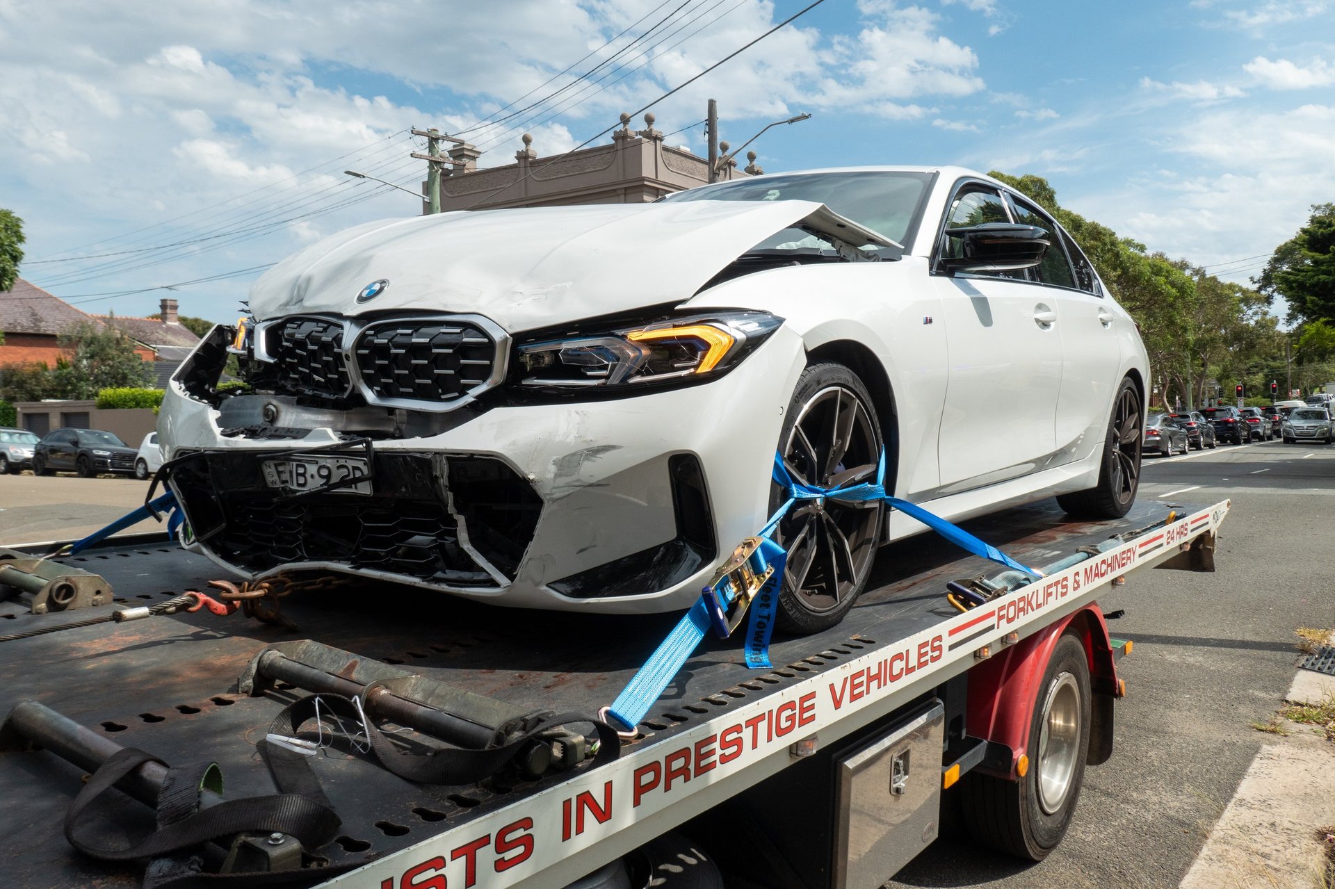 An electric BMW sedan on the back of a tow truck with emergency lights flashing