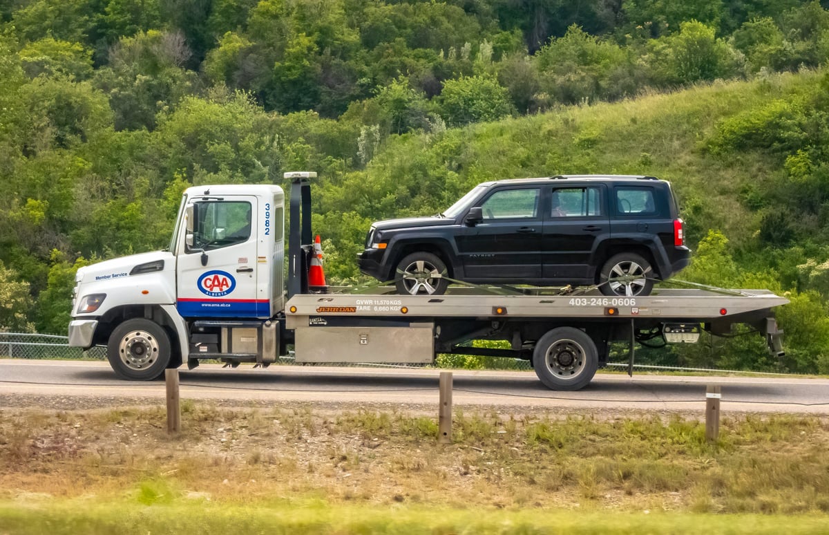 CAA flatbed tow truck carrying a black SUV on a road, symbolizing reliable roadside assistance