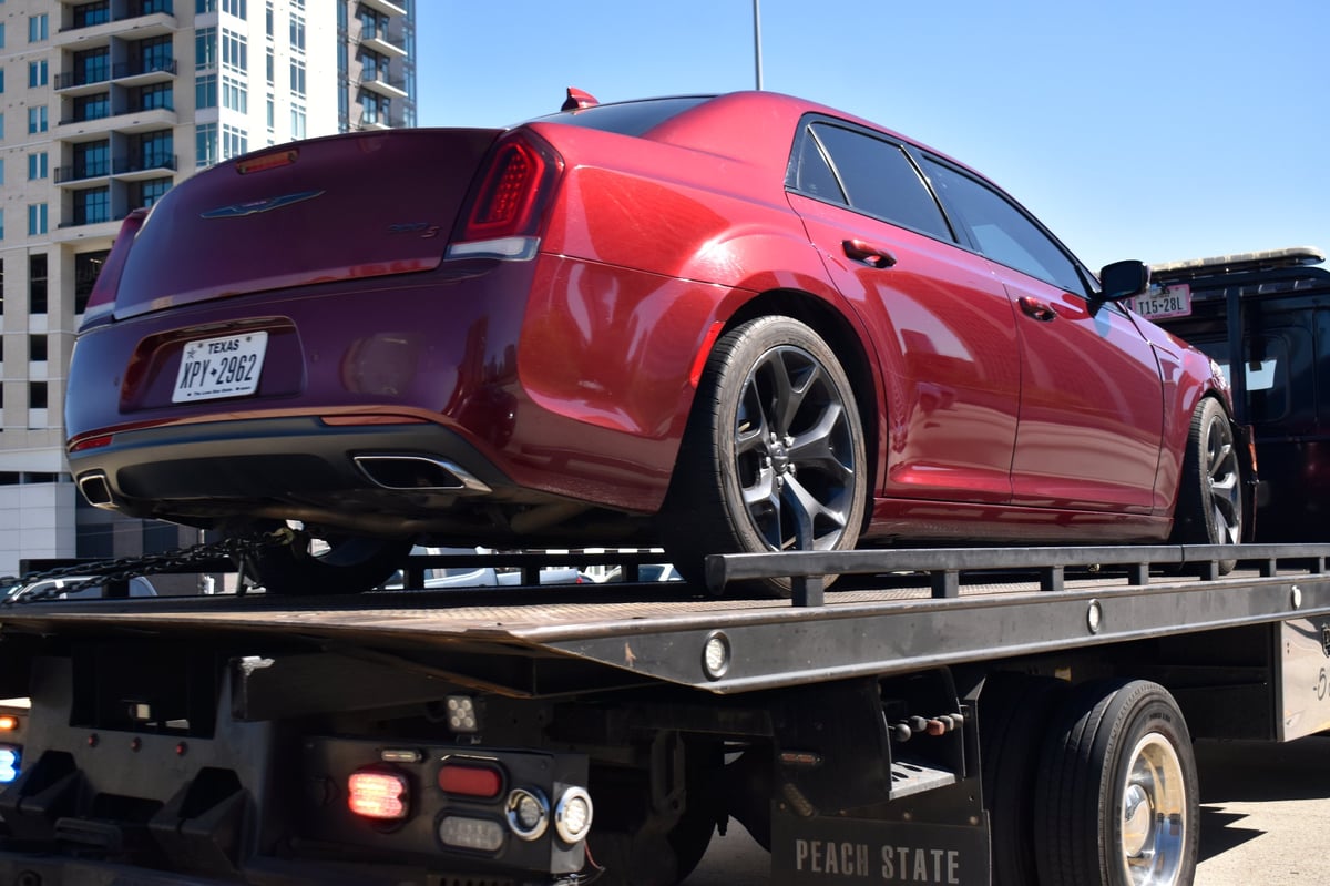 A red car with front-end damage loaded on a flatbed truck after an accident on the highway