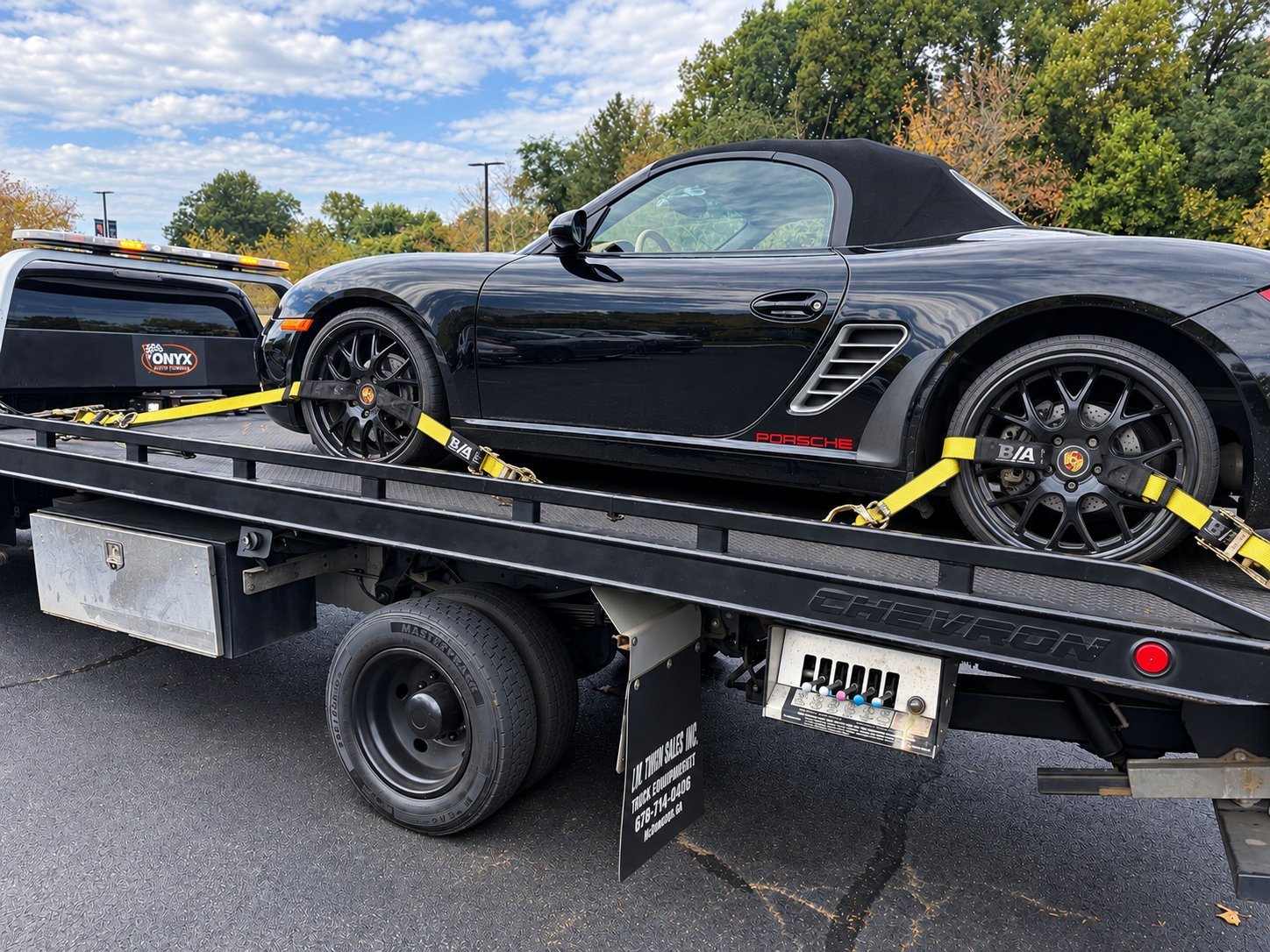 Black Porsche sports car secured with yellow straps on a flatbed tow truck during daytime