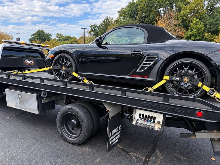 Black Porsche sports car secured with yellow straps on a flatbed tow truck during daytime