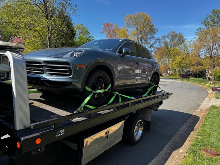 Dark SUV being towed on a flatbed truck with green straps, parked on a residential street in autumn
