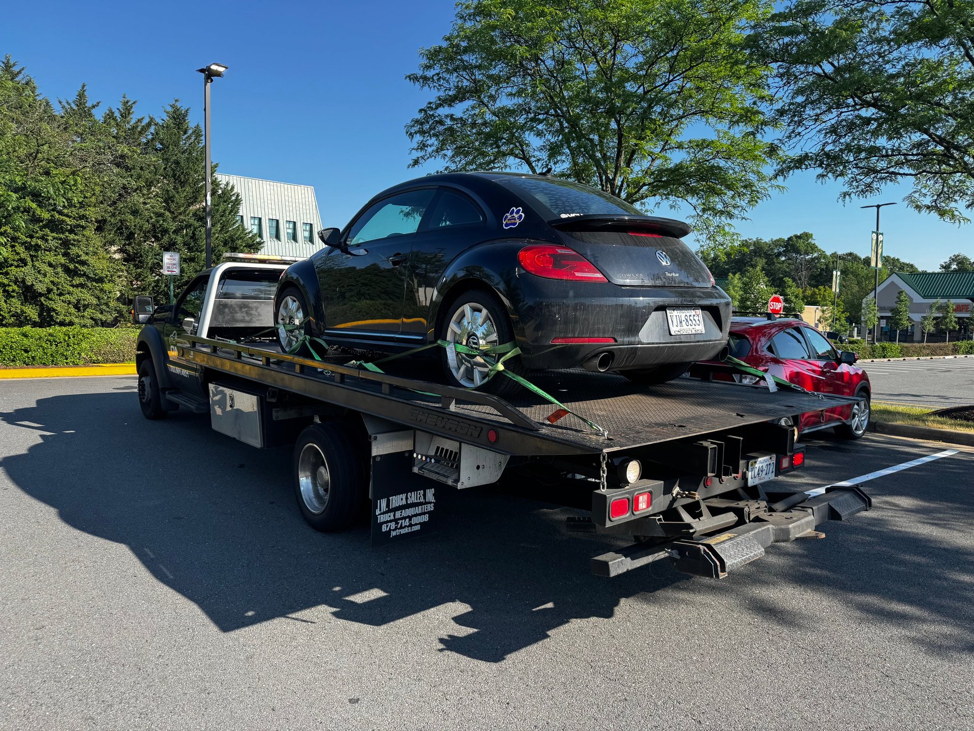 Black sedan and red compact car loaded on a flatbed tow truck in a parking lot on a sunny day