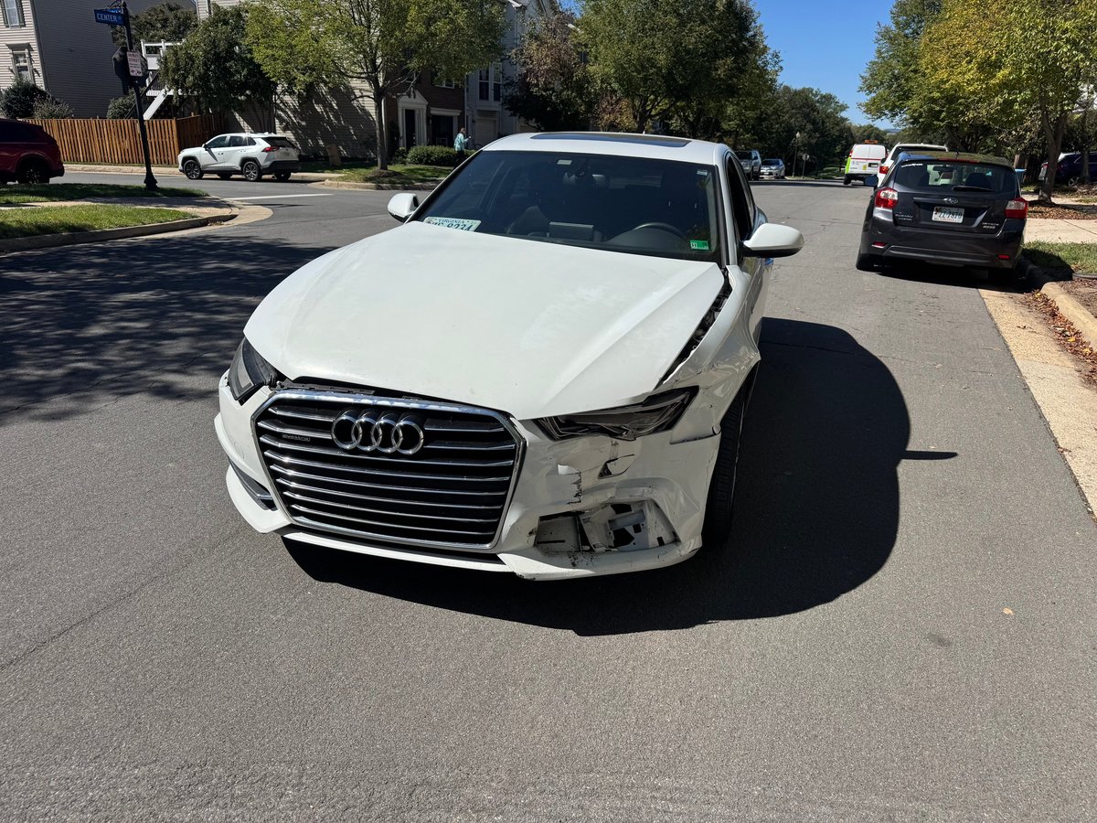 Damaged white Audi sedan with crumpled front end parked on residential street