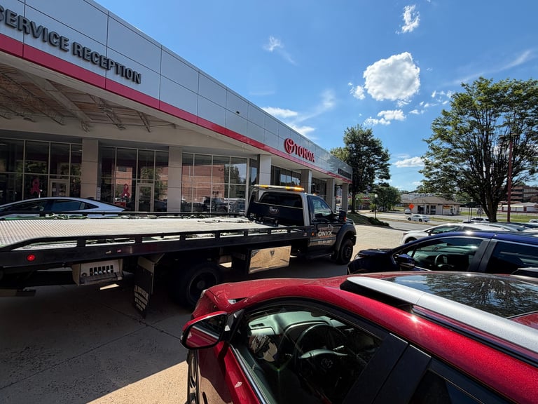 Tow truck parked outside auto repair shop with red car on flatbed and other vehicles in lot