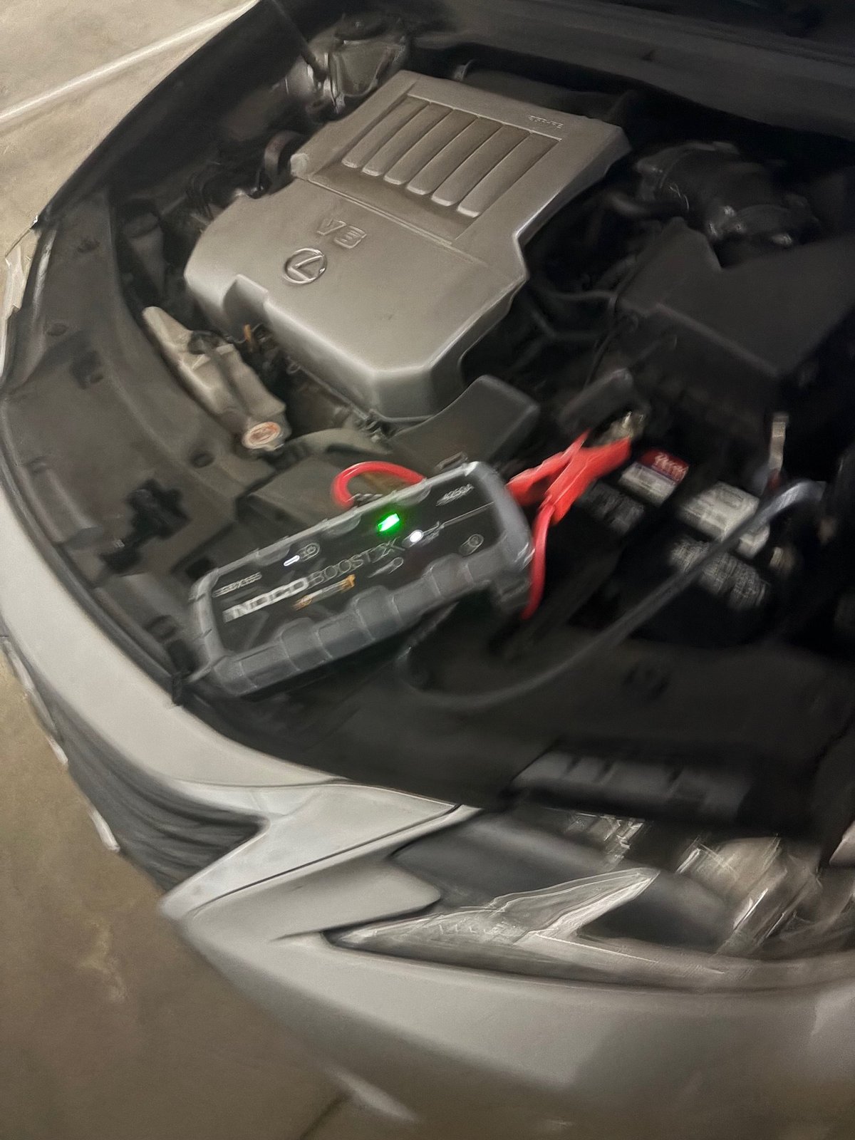 Car engine compartment showing silver engine cover, red jump starter cables, and black fuses on the right side