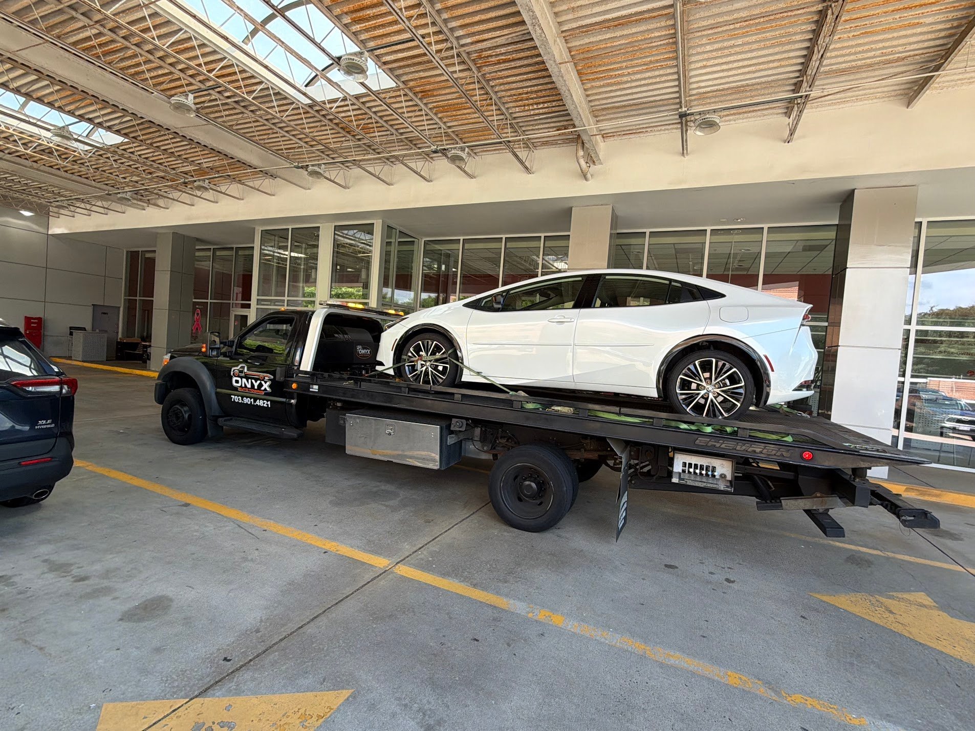 Black tow truck carrying a white luxury sedan in a covered garage or service facility