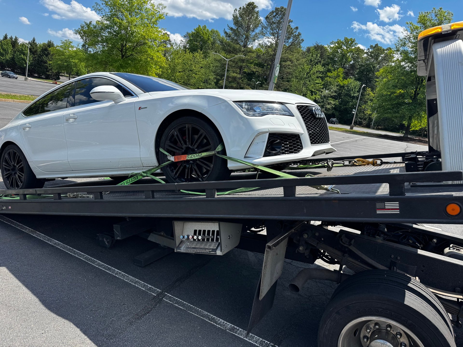 White Audi coupe secured on a flatbed tow truck with green tie-down straps