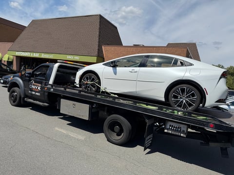 White sedan being towed on a flatbed truck with brick buildings in background