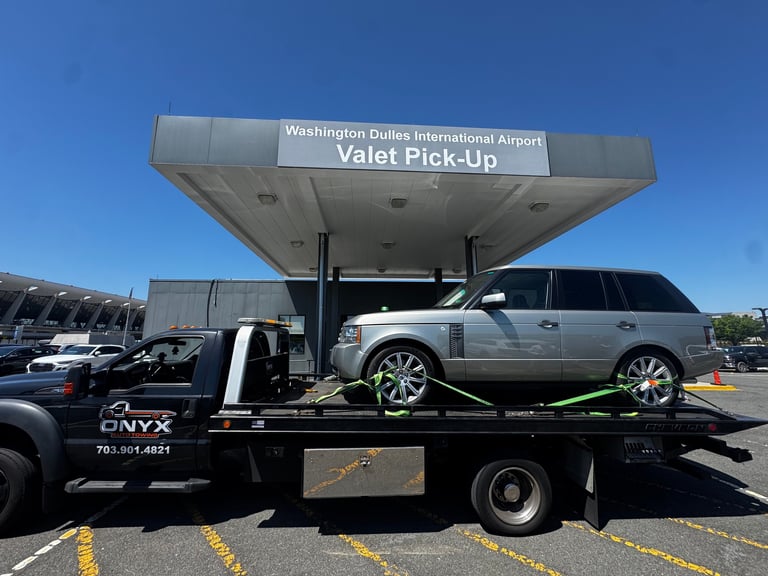 Silver SUV loaded on a flatbed tow truck at Washington Dulles International Airport valet pick-up area under blue sky