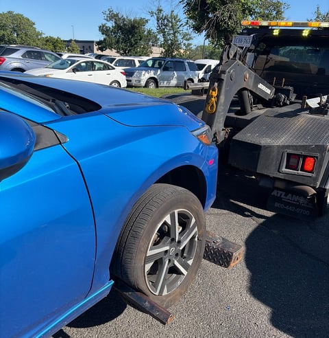 Blue car being loaded onto a black tow truck at a vehicle lot with other cars in the background
