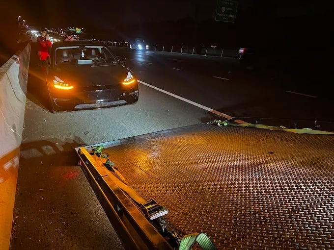 Car being towed at night on a flatbed truck with illuminated headlights and taillights on a highway