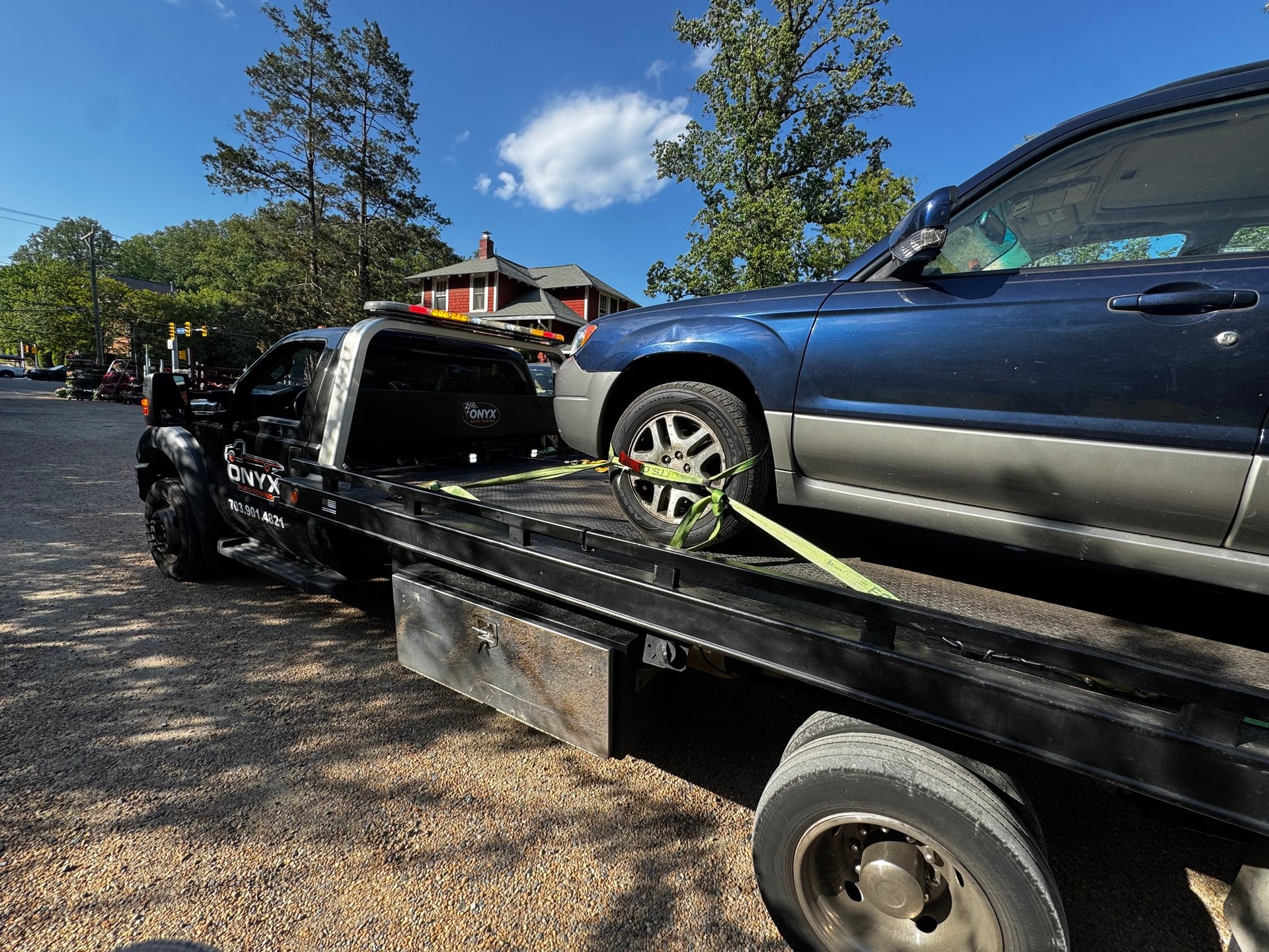 A blue SUV being loaded onto a black flatbed tow truck in a parking lot on a sunny day