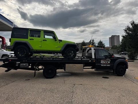 Bright green Jeep Wrangler being towed on a flatbed tow truck under overcast skies in an industrial area