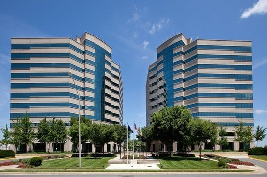 Two modern office buildings with blue and white striped facades and landscaped grounds under a clear blue sky