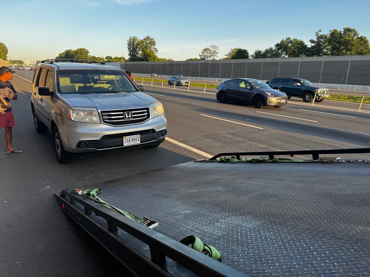 Silver Honda Pilot stopped on highway with roof rack visible in foreground and other vehicles in background