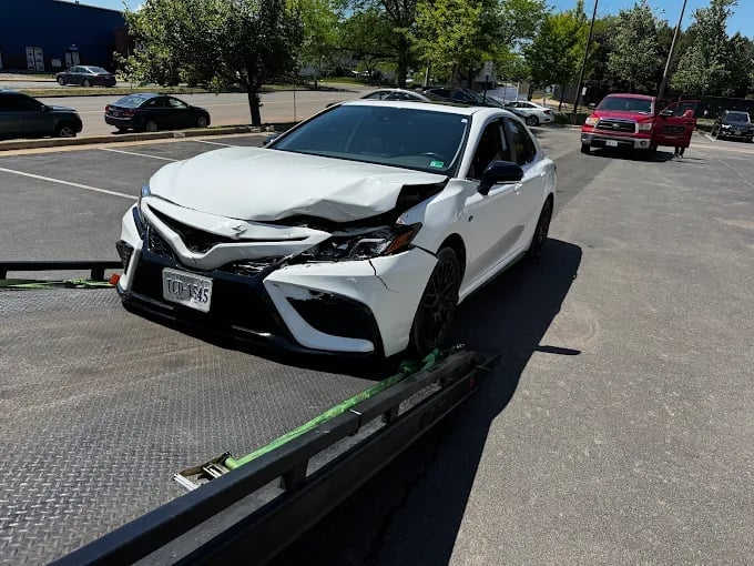 White Toyota Camry with front-end damage on a tow truck in a parking lot