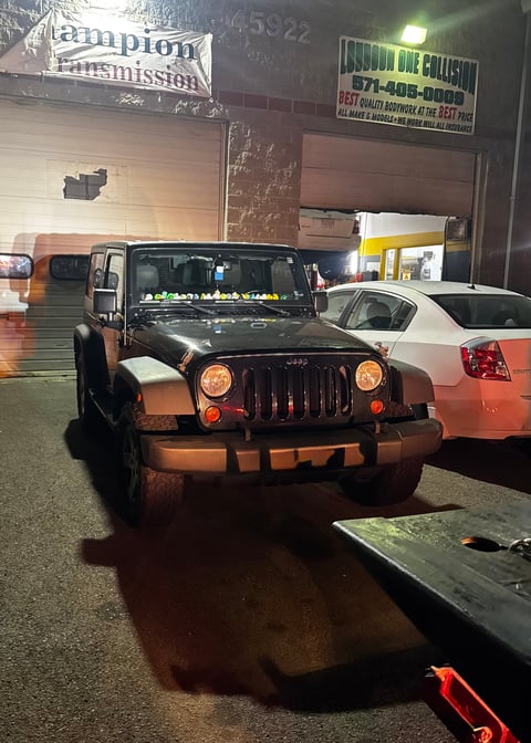 Black and tan Jeep Wrangler parked in an auto service garage at night with neon signs visible in background