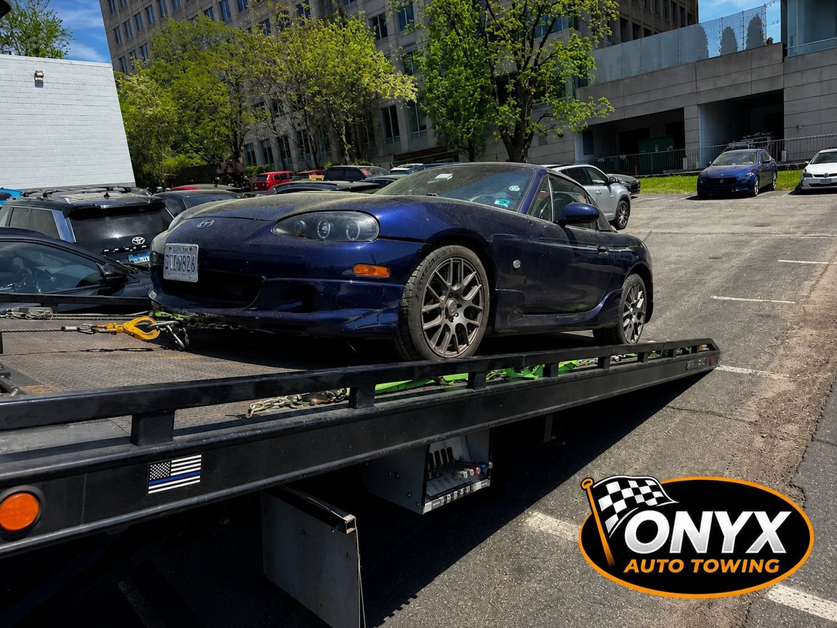 Blue sports car loaded on Onyx Auto Towing flatbed truck in urban parking area