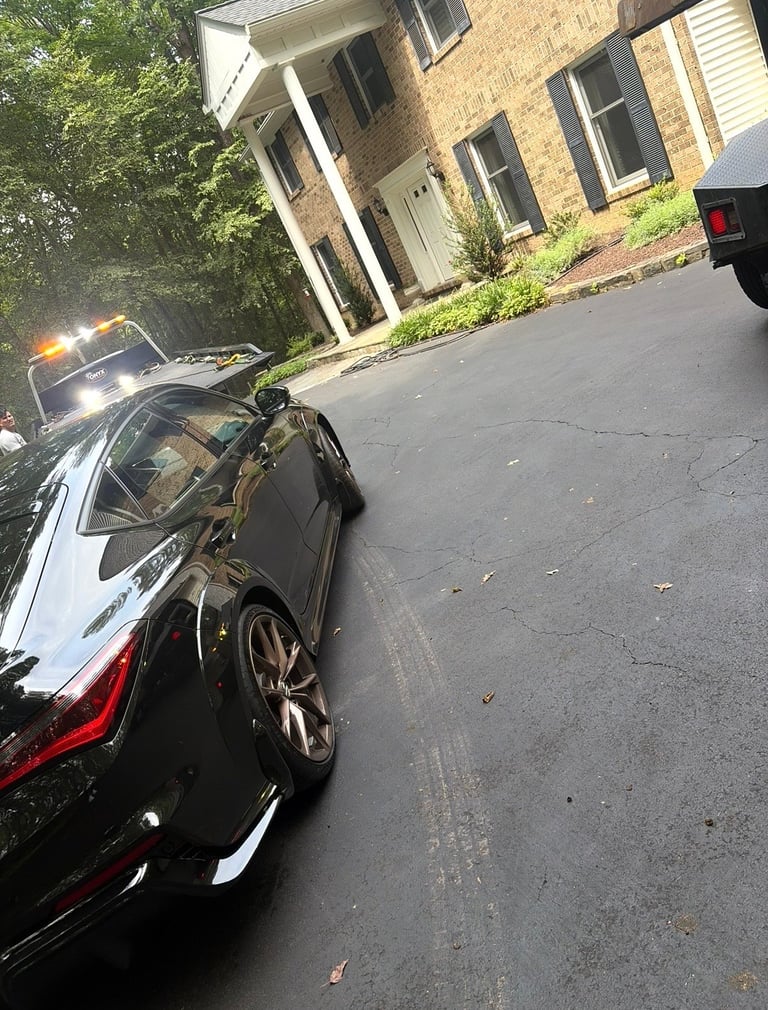 Black car parked in driveway in front of brick house with white trim and windows