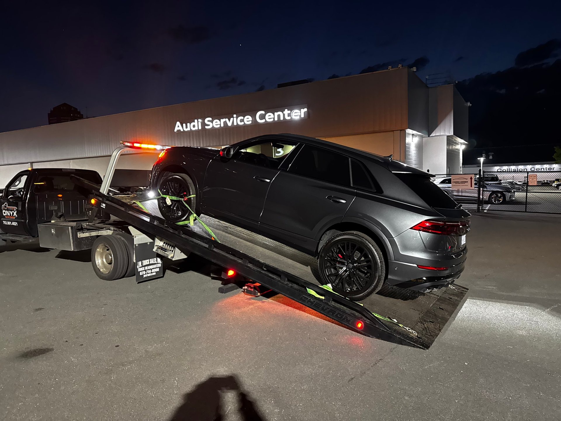Tow truck loading a black Audi vehicle at night outside an Audi Service Center