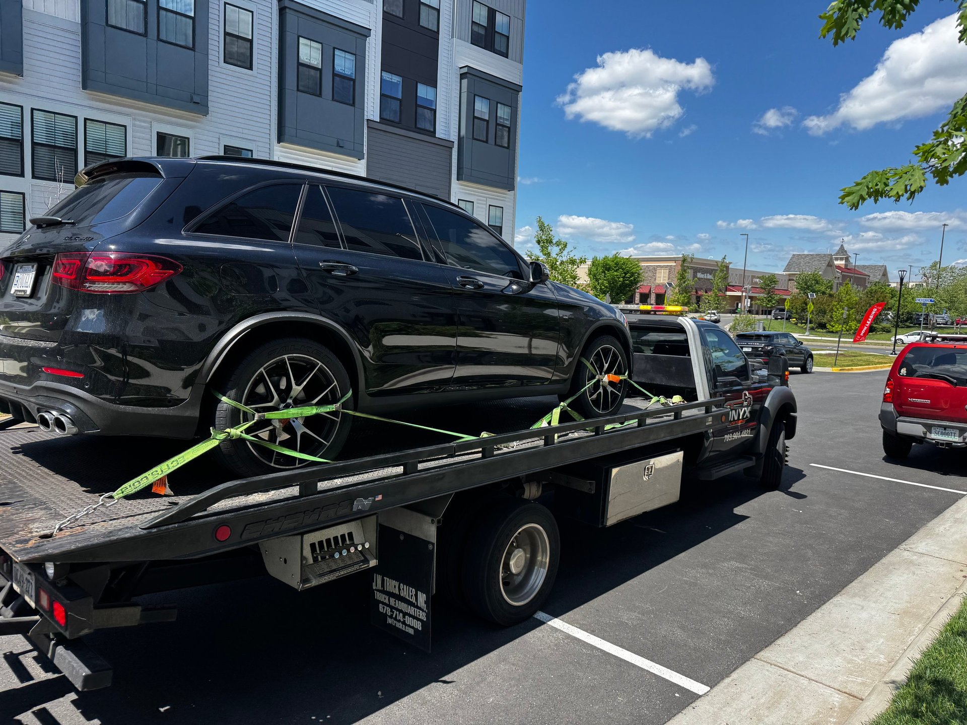 Black SUV being towed on a flatbed tow truck in a parking lot on a sunny day