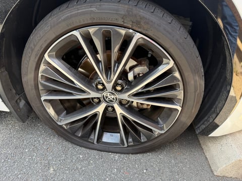 Close-up of a vehicle wheel with a silver and black multi-spoke alloy rim and gray tire on concrete surface