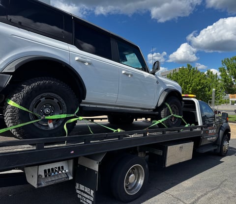 White SUV being towed on a flatbed truck with neon green straps securing it in place
